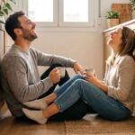 Couple laughing on kitchen floor with coffee.