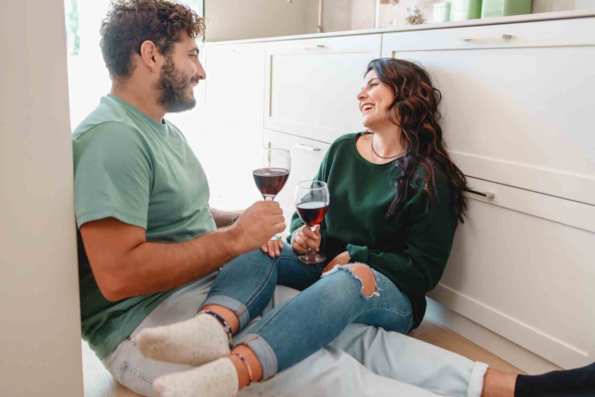 Couple enjoying wine on kitchen floor, laughing together